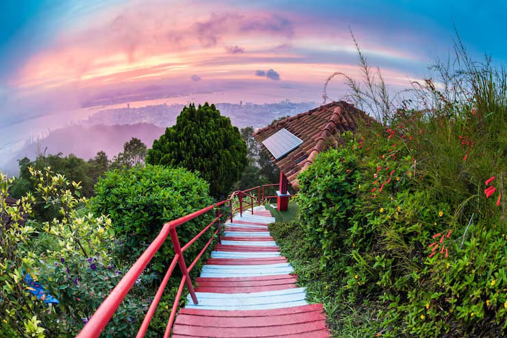 Colorful stairs leading up a lush hill with a sunset city view in the background