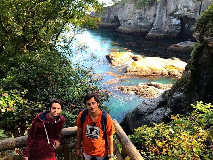 Two travelers standing on a wooden lookout overlooking a rocky ocean cove