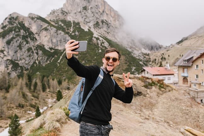 Excited hiker taking a selfie with scenic mountain peaks in the background