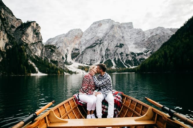 Couple sharing a romantic kiss in a rowboat on a scenic mountain lake