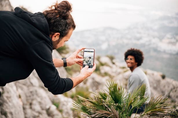 Friends hiking on a rocky mountain trail taking photos with a smartphone